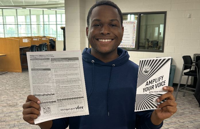  student smiling holding a voter application and information pamphlet